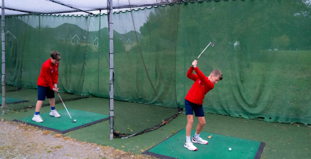 Boys practicing golf swings in a driving range, wearing red shirts and focusing on technique.