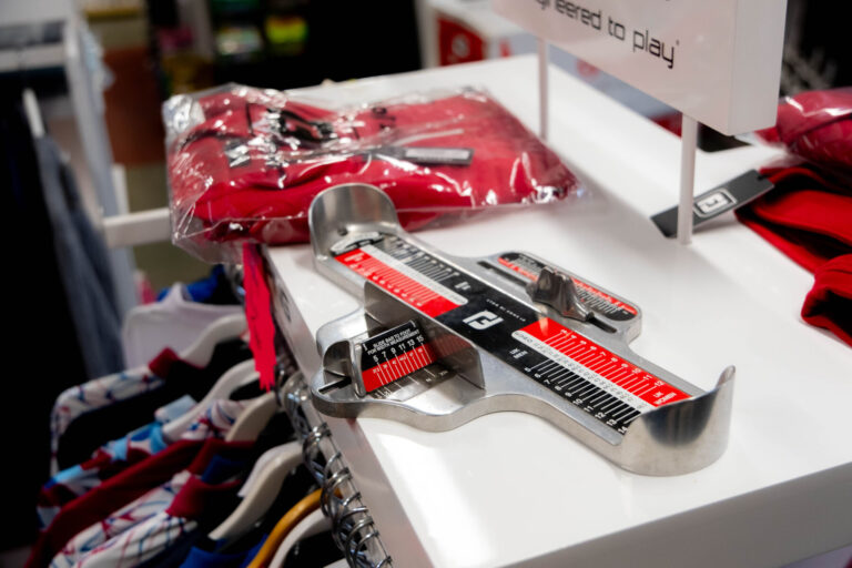 Brannock device on display counter with red clothes and hangers in a store setting.