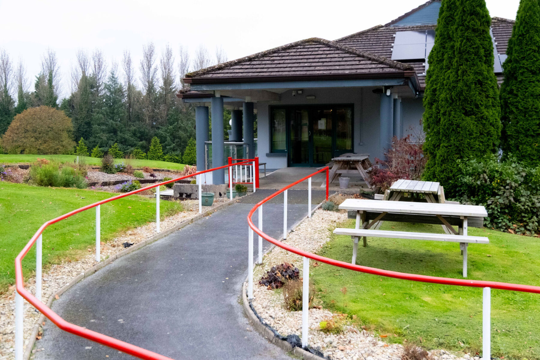 Wheelchair-accessible ramp leading to a building surrounded by greenery and picnic tables.