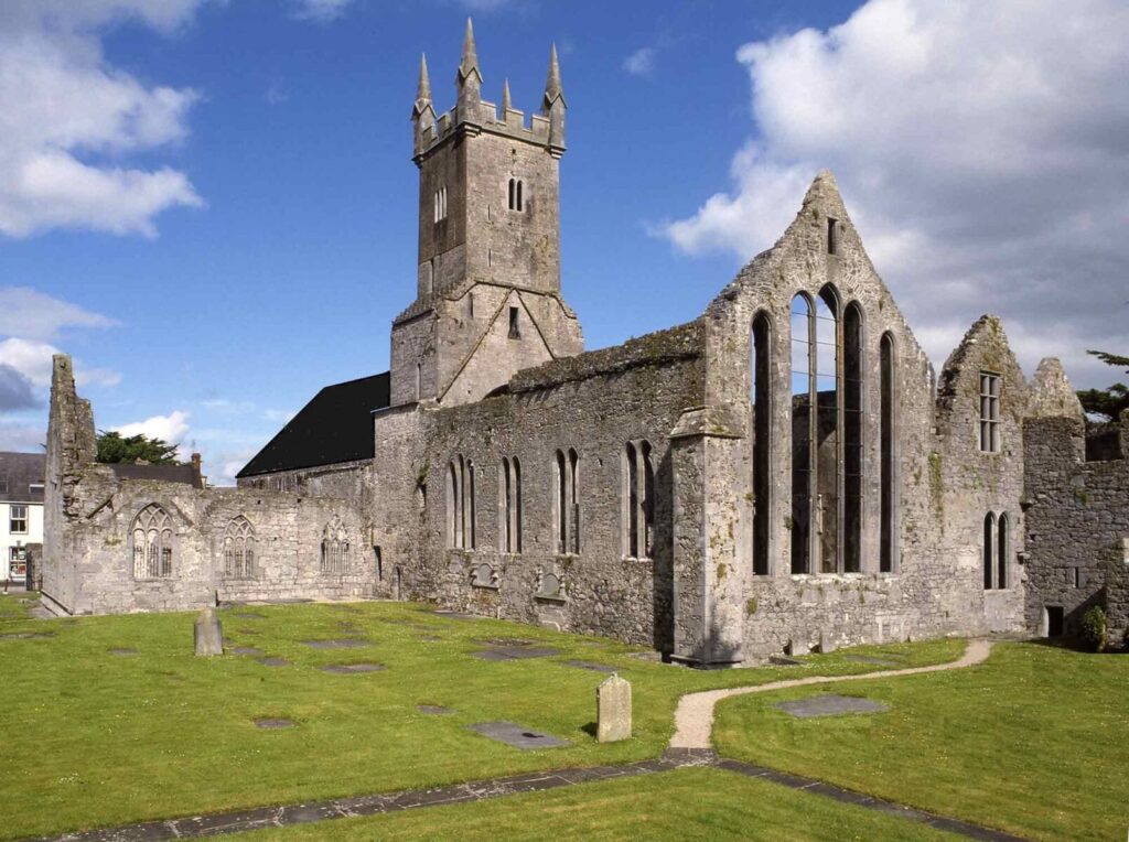 Ancient stone church with tower under a blue sky, surrounded by green grass and pathways.
