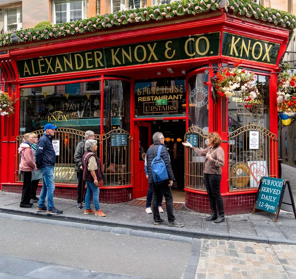 People standing outside a vibrant red pub named Alexander Knox & Co in a lively street setting.