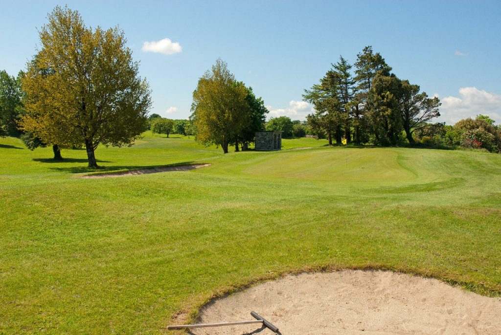 Scenic golf course with green fairways, sand bunker, and trees under a blue sky. Perfect for golf enthusiasts.