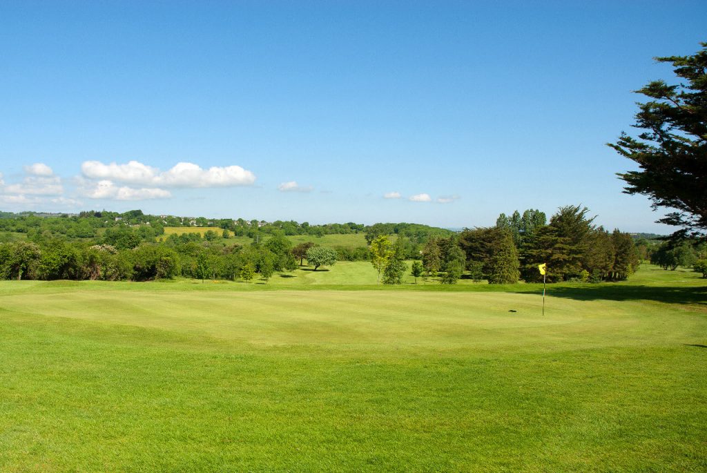 Scenic golf course with green fairway, trees, and blue sky. Ideal golfing destination for nature lovers.