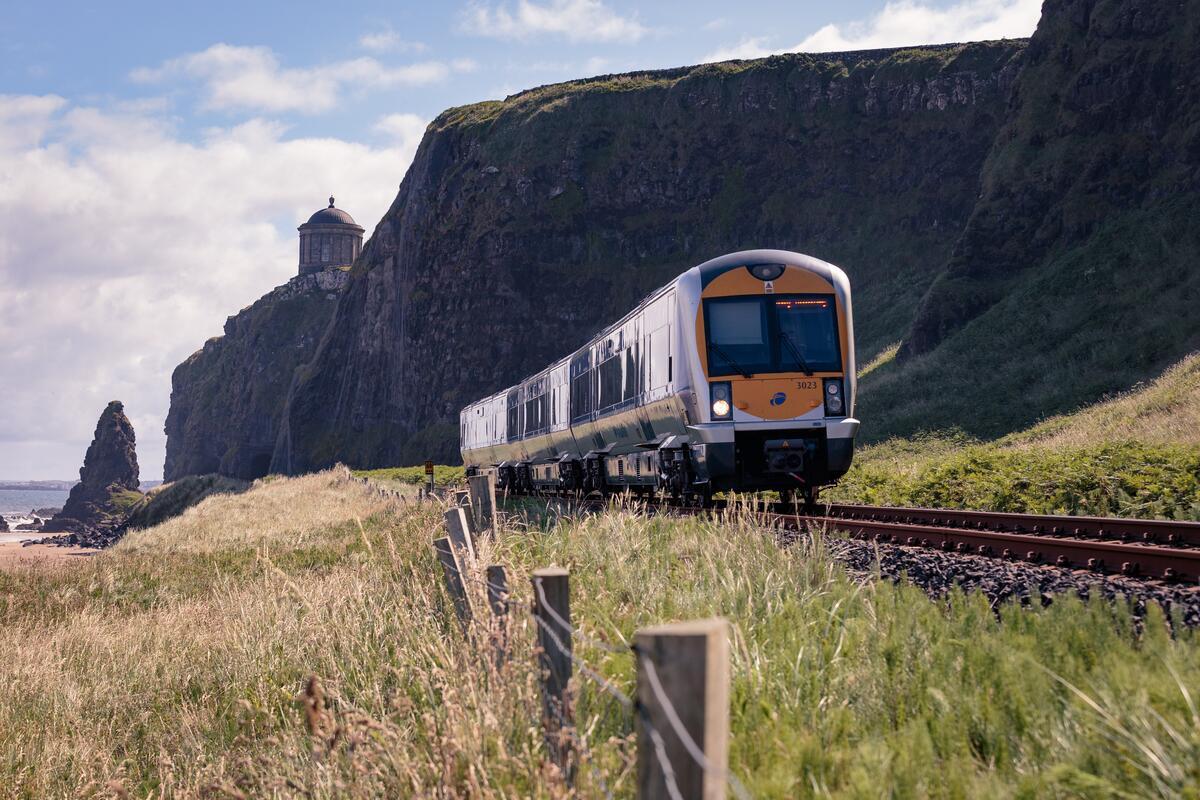Train passing scenic cliffs and coastal landscape under a cloudy sky.
