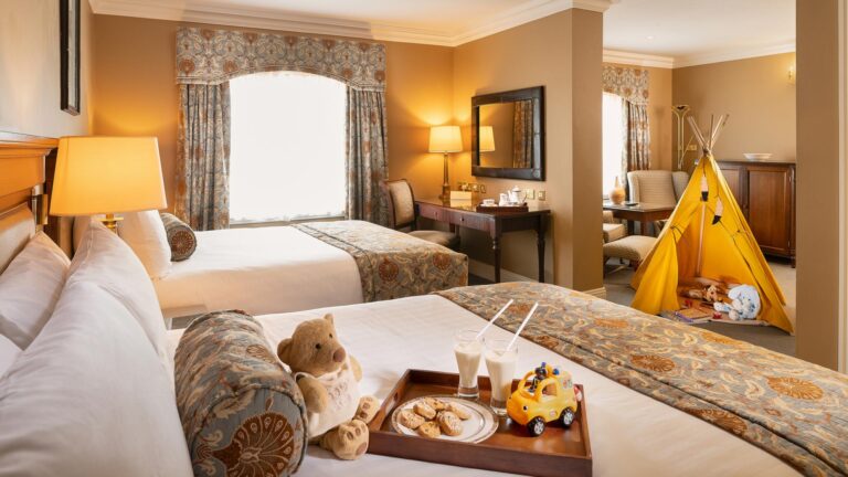 Luxurious family hotel room with cozy beds, teddy bear, toy car, and a kids' play tent for a comfortable stay.