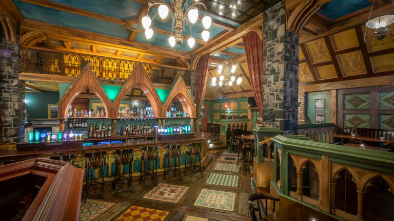 Rustic pub interior with wooden beams, ornate bar, and vintage lighting creating a cozy ambiance.