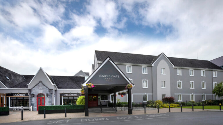 Facade of Temple Gate Hotel with clear skies, featuring Legends and Preacher's shops on the left.