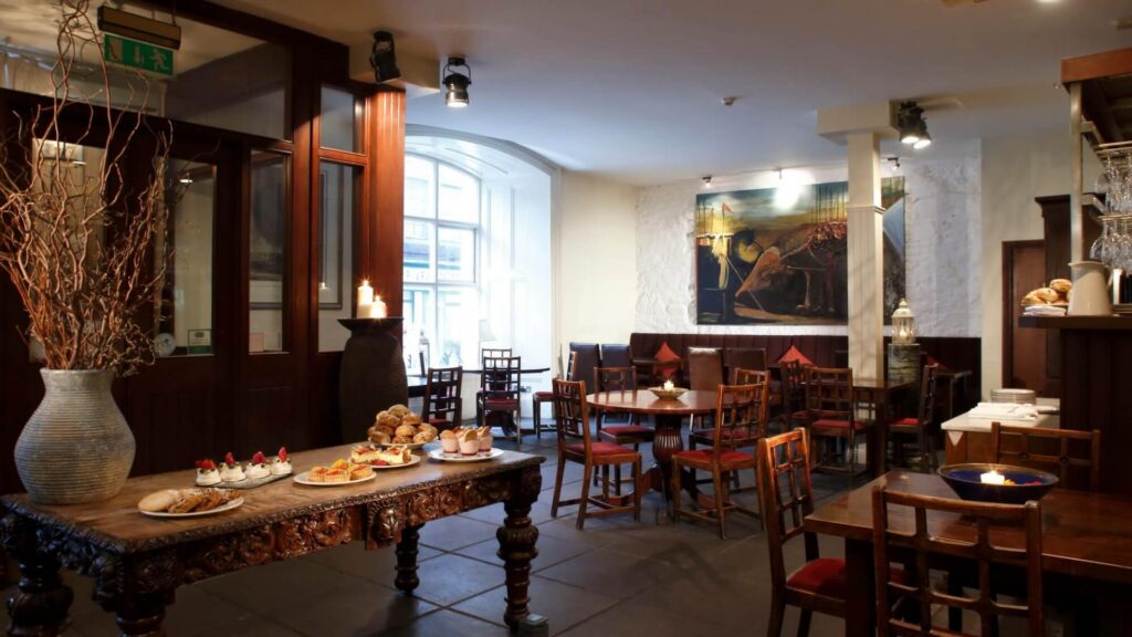 Cozy restaurant interior with ornate furniture and assorted pastries on a table, under warm lighting.