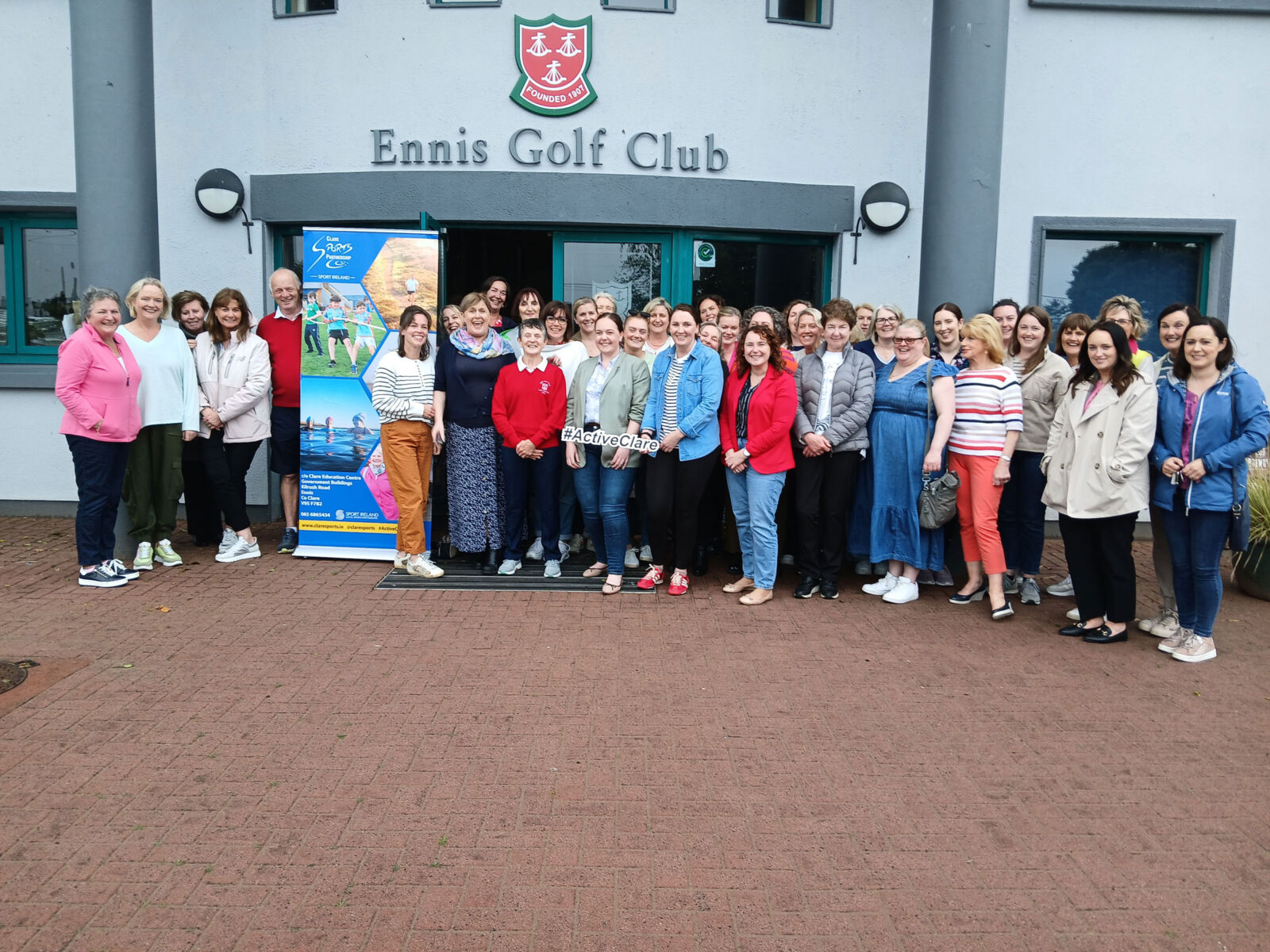 Group of people gathered outside Ennis Golf Club for a community event, promoting local activities, smiling and engaged.