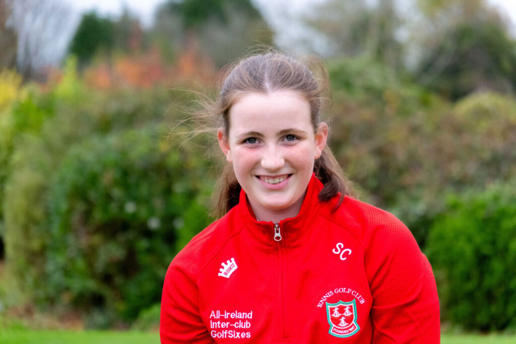 Young person in a red Ennis Golf Club jacket outdoors, smiling at the camera.