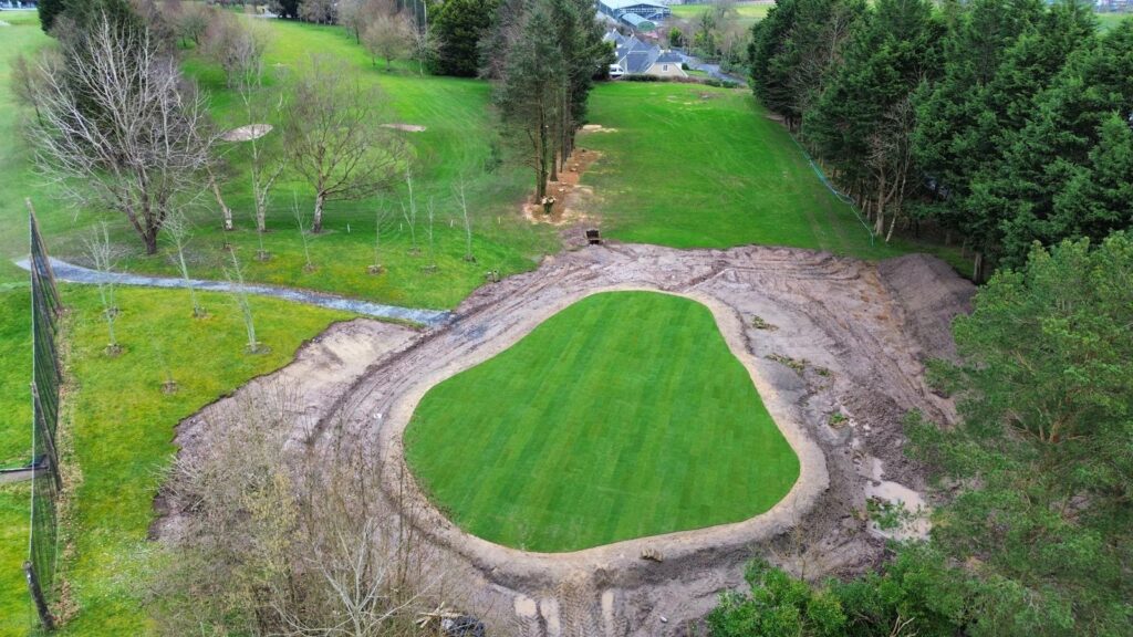 Aerial view of a golf course construction site with green, trees, and dirt paths.
