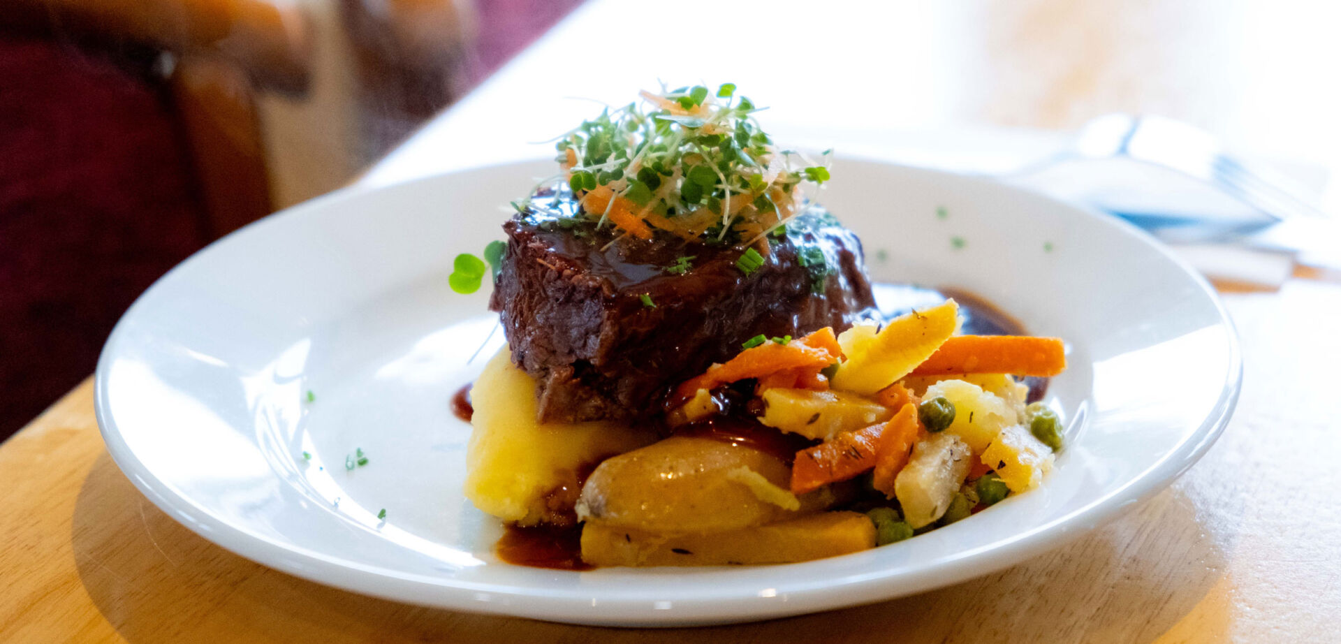 Gourmet dish with tender beef, creamy mashed potatoes, and colorful vegetable medley on a white plate.