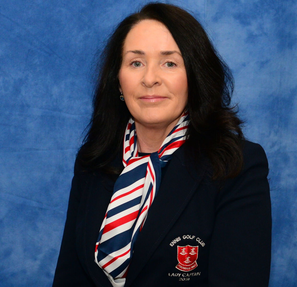 Portrait of a woman in a navy blazer with Lady Captain 2020 logo, wearing a striped scarf and smiling.