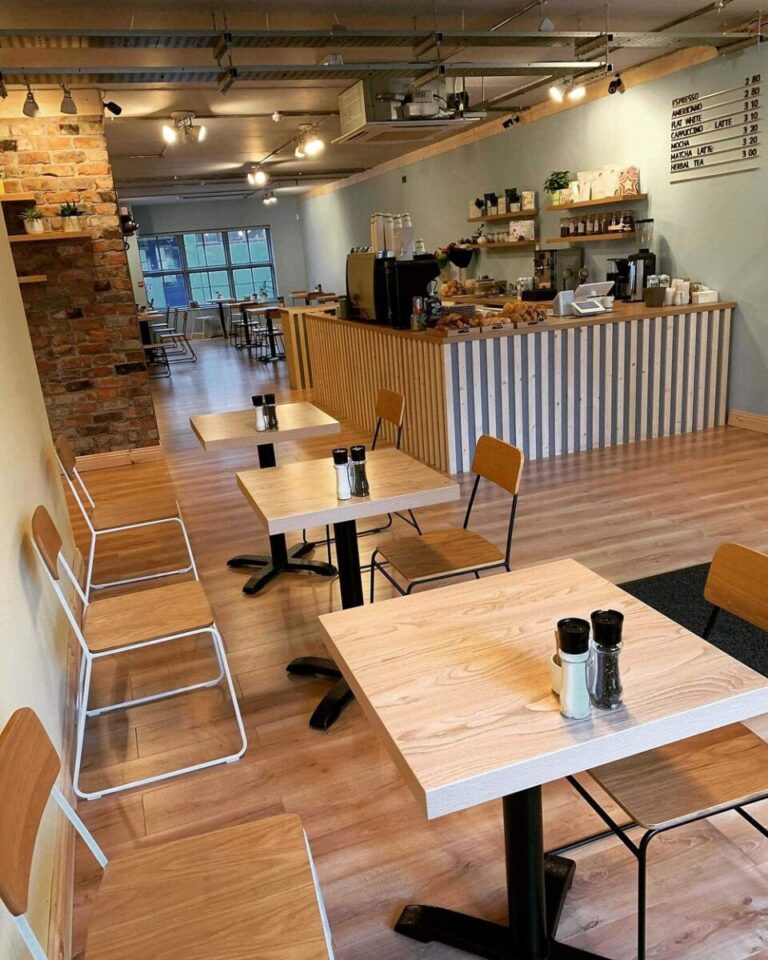 Cozy modern cafe interior with wooden tables, chairs, and a counter displaying menu items in a welcoming atmosphere.