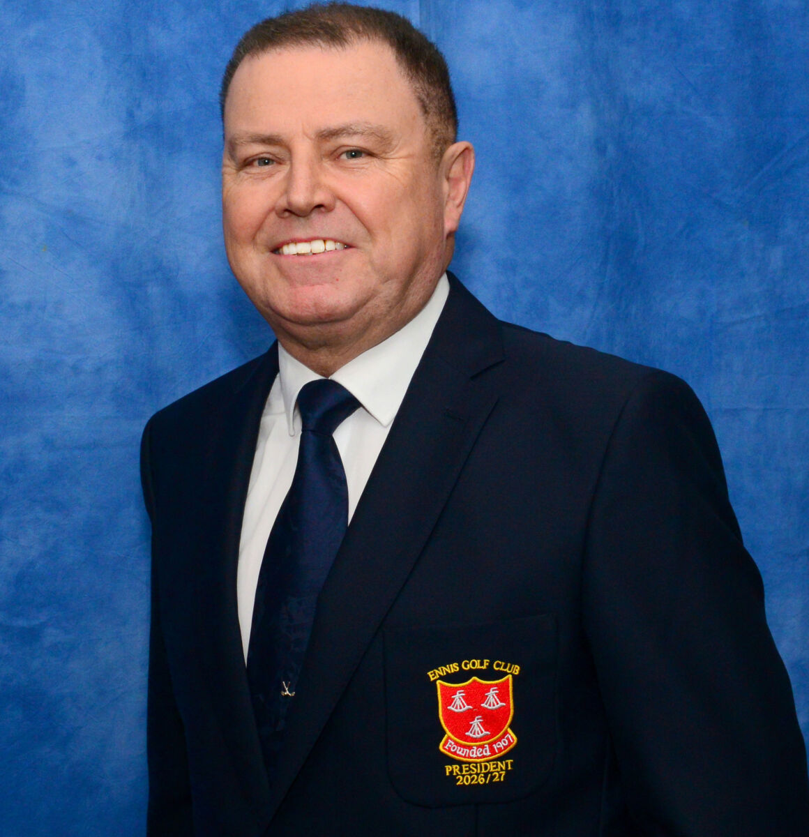 Man in a blue suit smiling, wearing an Ennis Golf Club badge with President 2026/27 on a blue background.