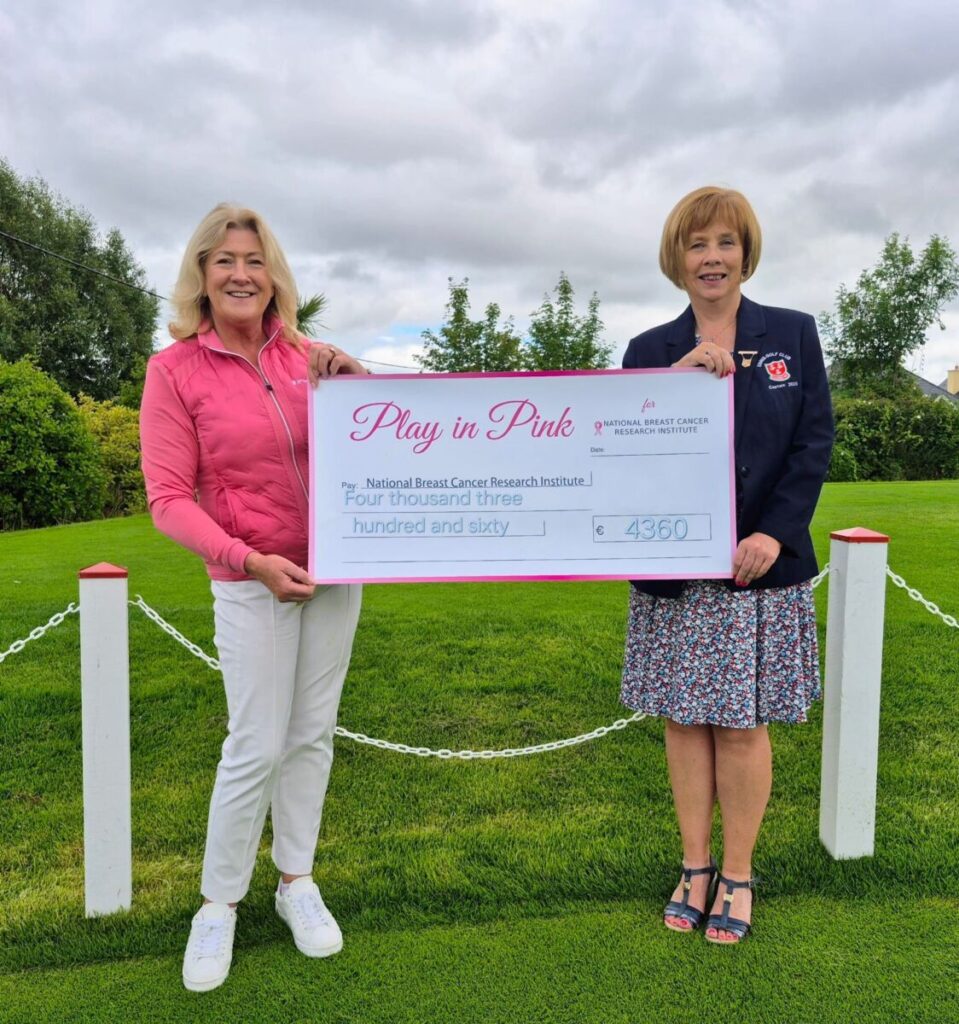 Two women holding a large donation check for €4360 to the National Breast Cancer Research Institute in a garden setting.
