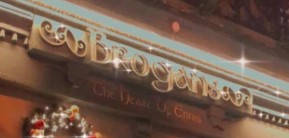 Close-up of a festive storefront sign reading Brogans adorned with holiday decorations and bright lighting.