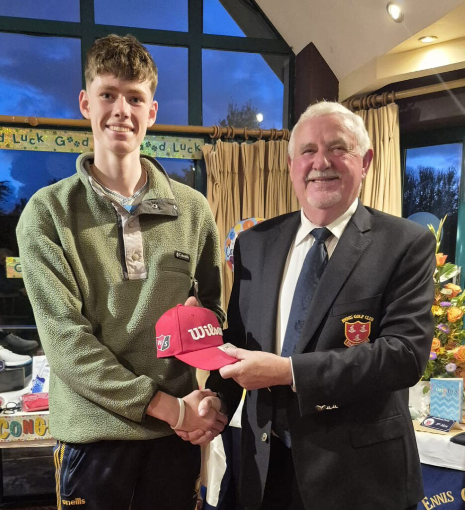 Young man receiving red Wilson cap from older man at celebratory event, handshake and smiles.
