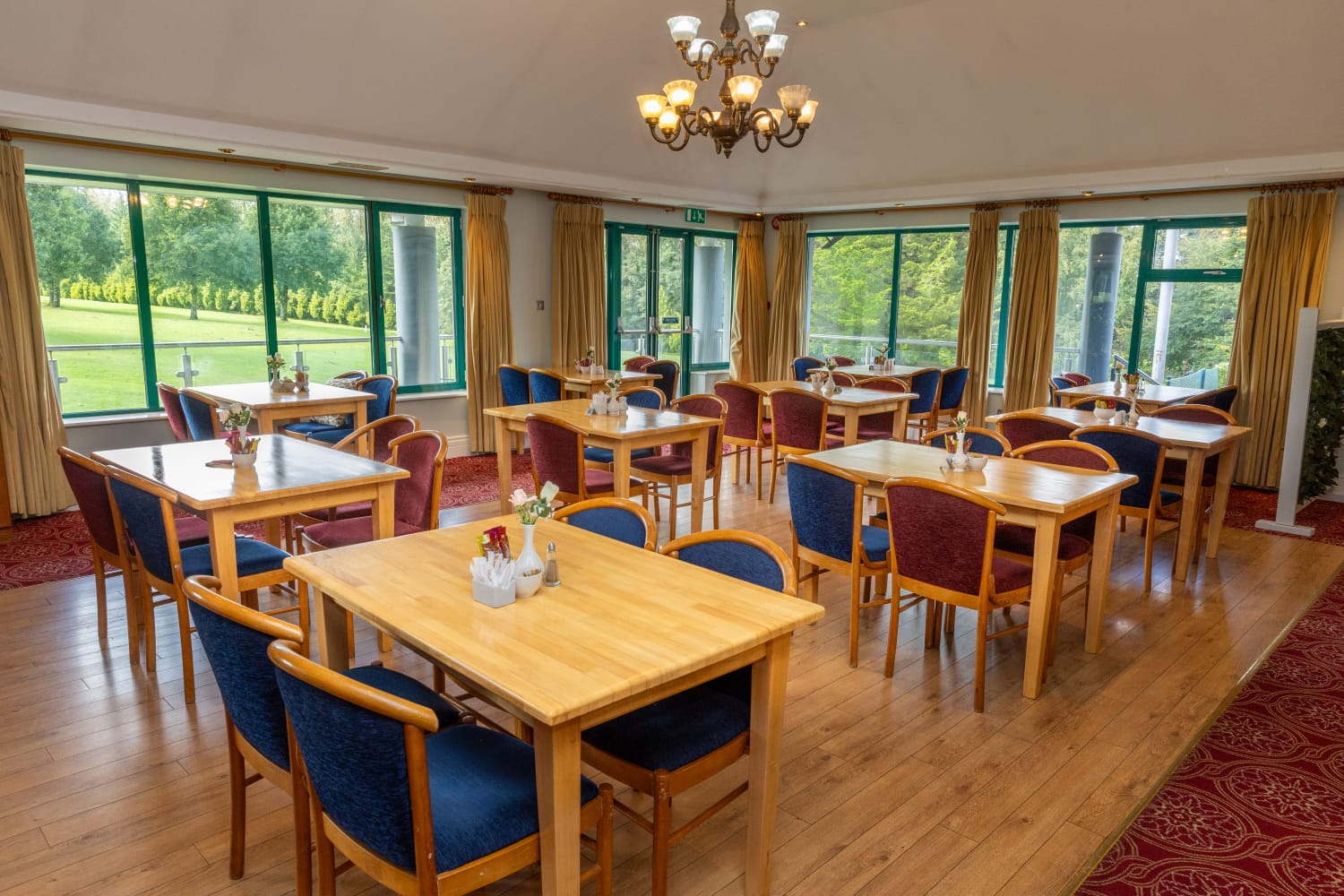 Elegant dining room with wooden tables and chairs, large windows, and scenic garden view. Perfect for a relaxing meal.