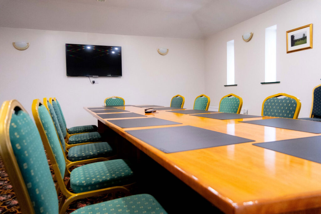 Modern conference room with green chairs, a wooden table, and a wall-mounted screen. Ideal for meetings and presentations.