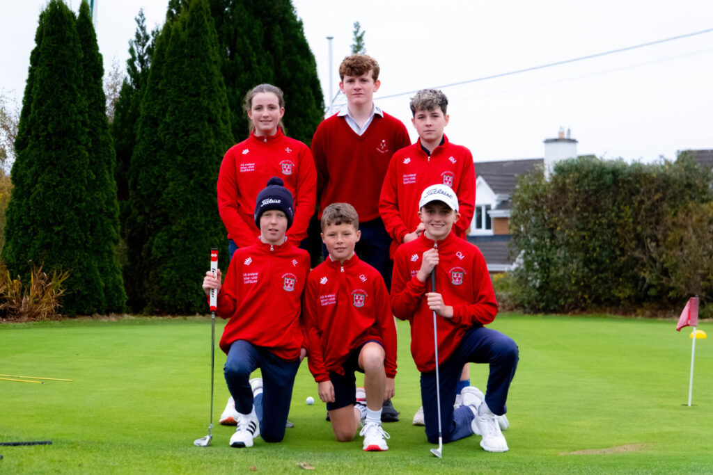 Youth golf team in red uniforms kneeling and standing on a green.