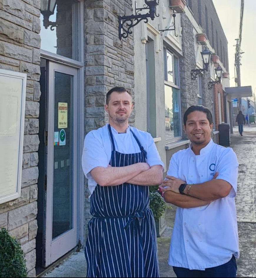 Two chefs in uniform standing outside a stone restaurant building, showcasing culinary expertise.