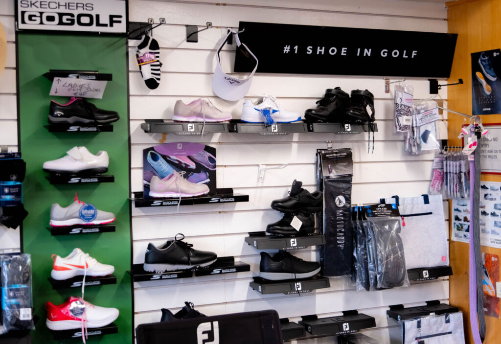 Golf shoes displayed on a wall in a store, featuring various brands and styles for men and women.